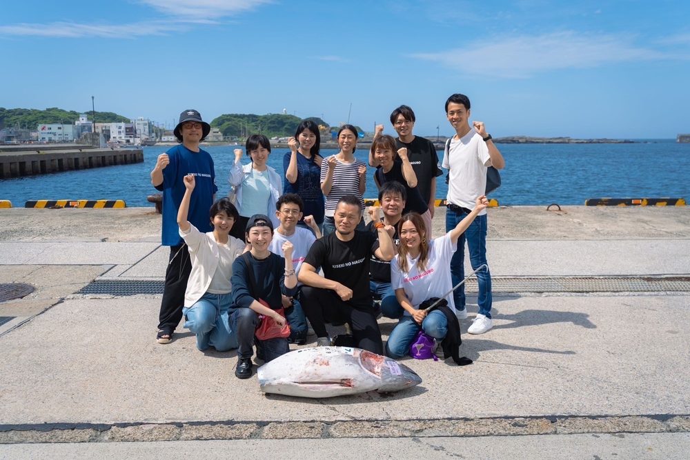 港で勝ち取ったマグロを囲み全員でガッツポーズする社員たち